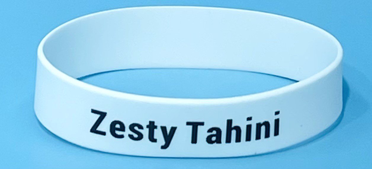 A white bracelet with the words zesty tahini written on it.