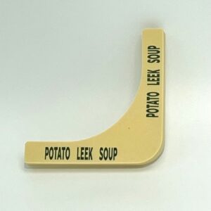 A yellow potato leek soup sign on the side of a white table.