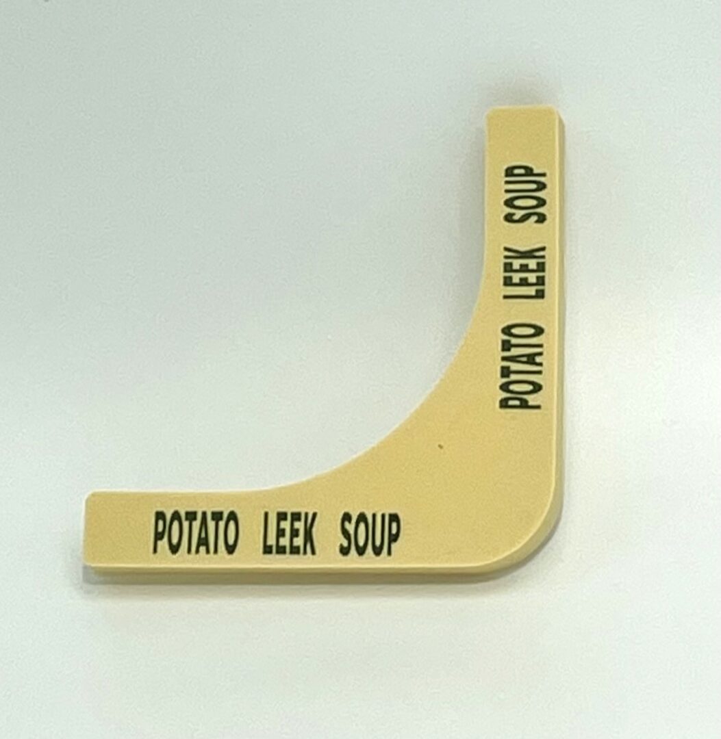 A yellow potato leek soup sign on the side of a white table.