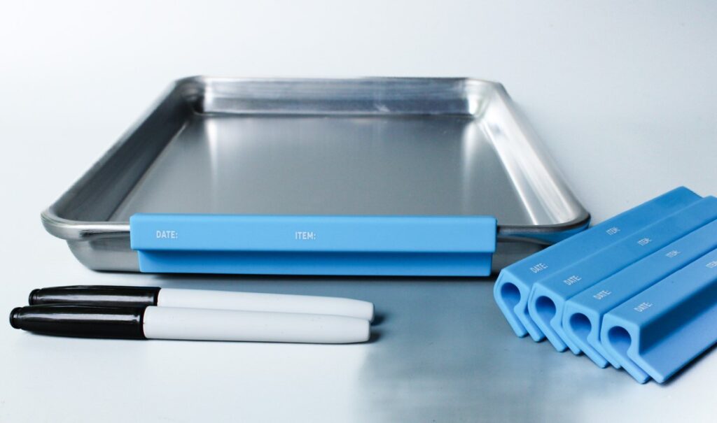 A metal tray with blue handles and two white markers.